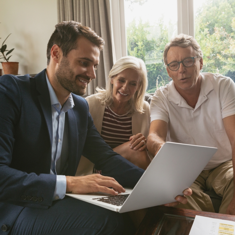 Active senior couple discussing with real estate agent over laptop in living room